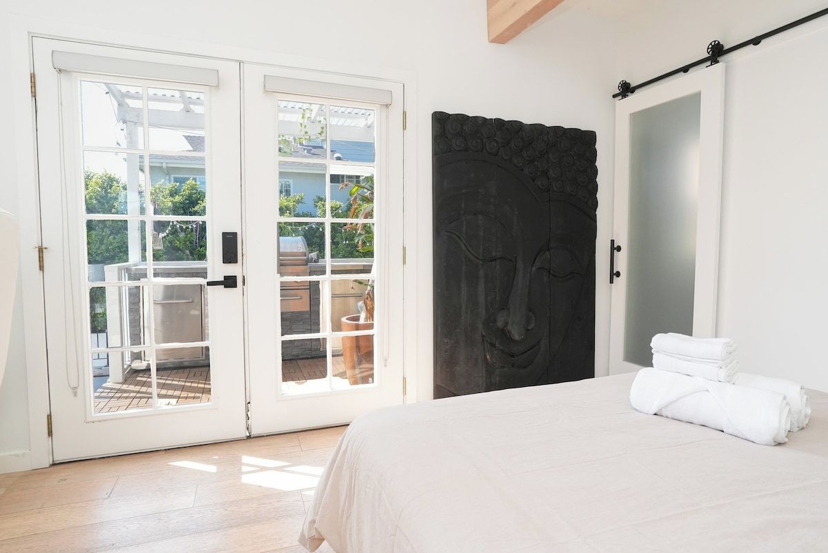 Un dormitorio con una cama, una puerta oscura grande y un ventanal corredero que da a un espacio exterior.