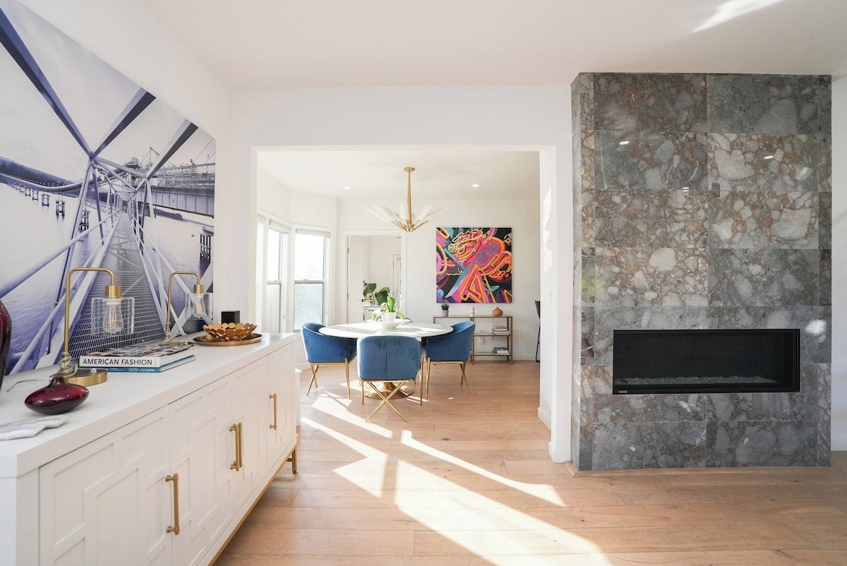 Una cocina moderna con encimera blanca, sillas azules y un cuadro abstracto grande en la pared.