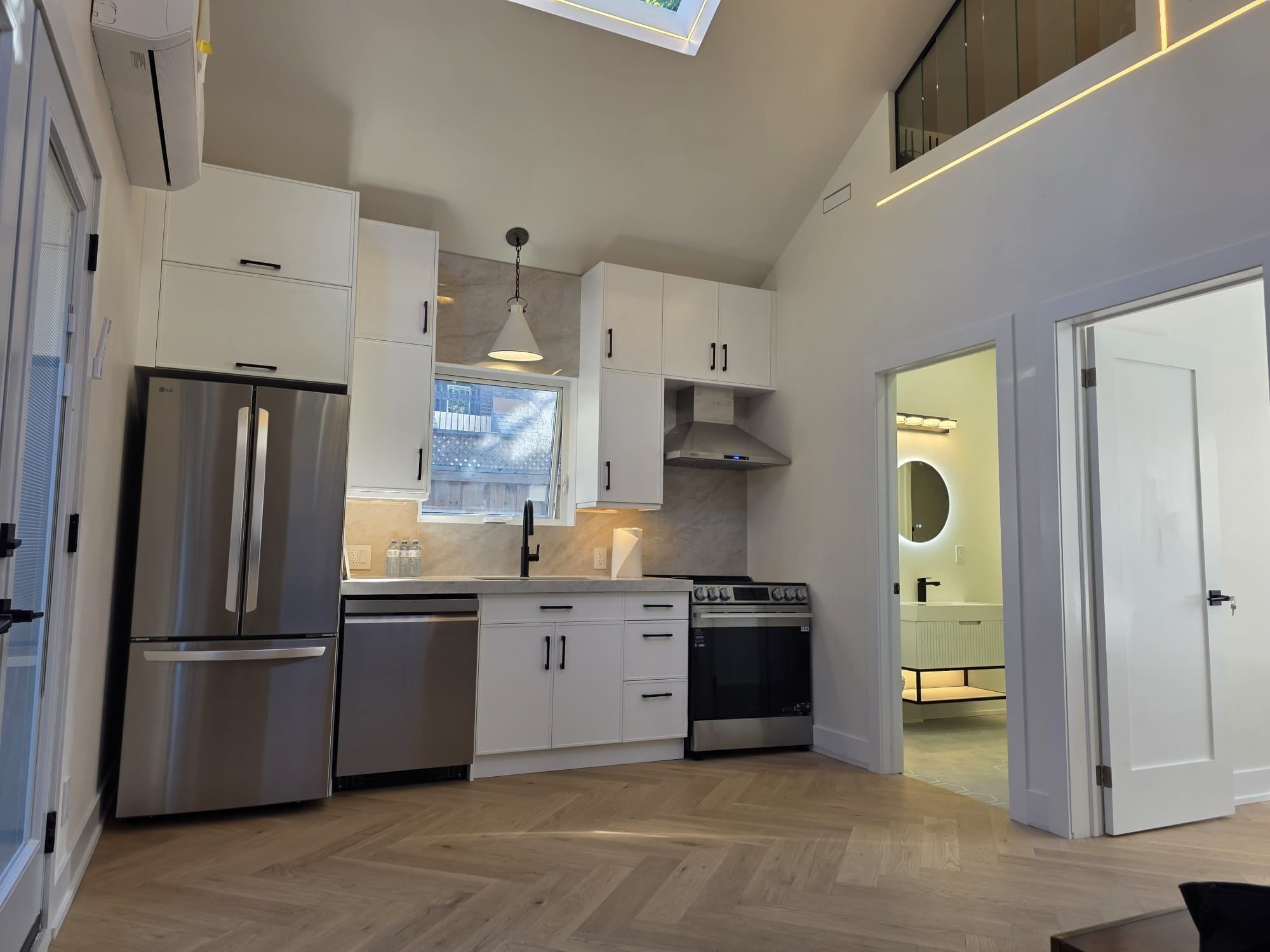 A modern kitchen with stainless steel appliances, white cabinetry, and a herringbone wood floor.