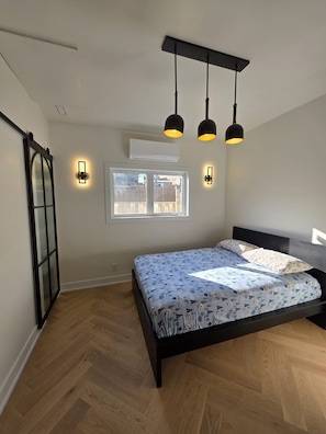 Et soveværelse med seng, et vindue, en aircondition og en loftlampe.
