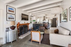 A spacious living area with a fireplace, a sofa, a coffee table, and a television mounted on the wall. - Cowboy Tubs, Quiet, Zen, Stars-1 bd + Studio (Joshua Tree)