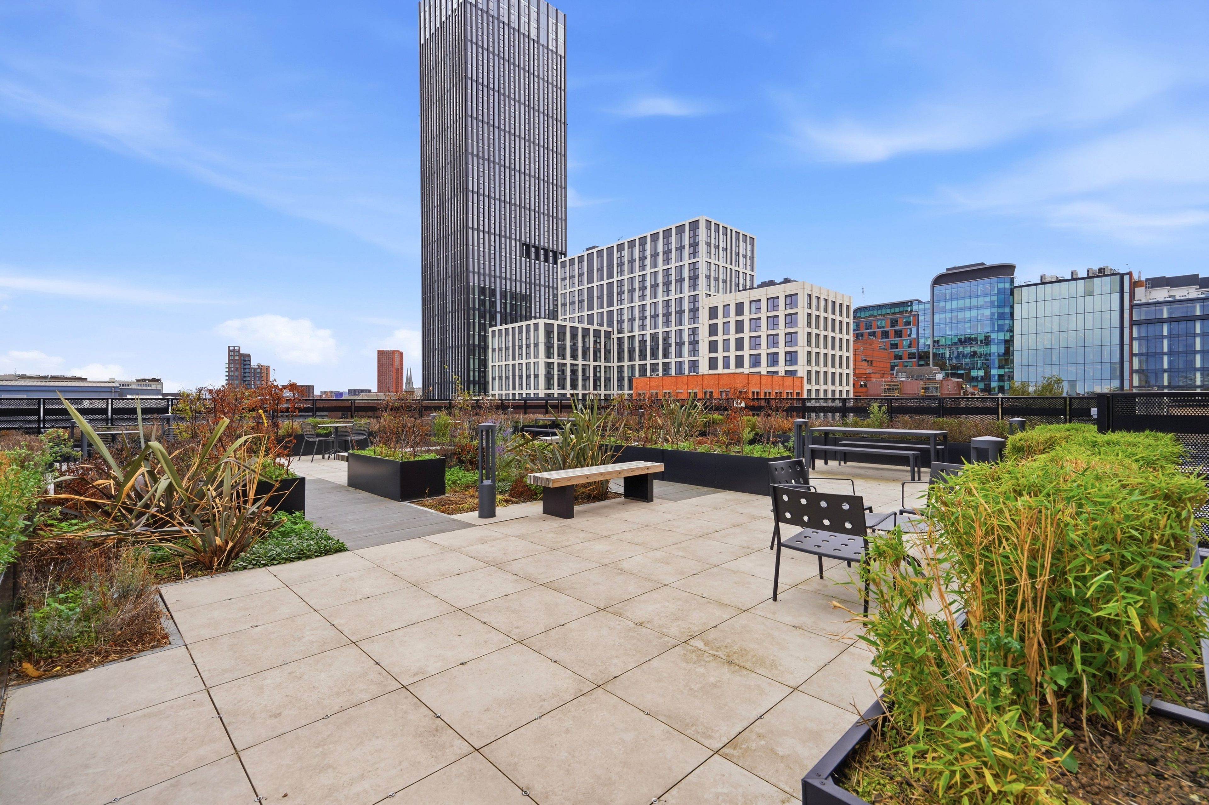 Une terrasse sur le toit, aménagée avec des sièges, des plantes et offrant une vue sur des bâtiments modernes.