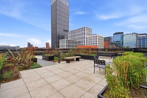 A rooftop terrace with seating, plants, and a view of modern buildings. - 2-Bed Apartment Jewellery Quarter - Rooftop Garden (West Midlands)
