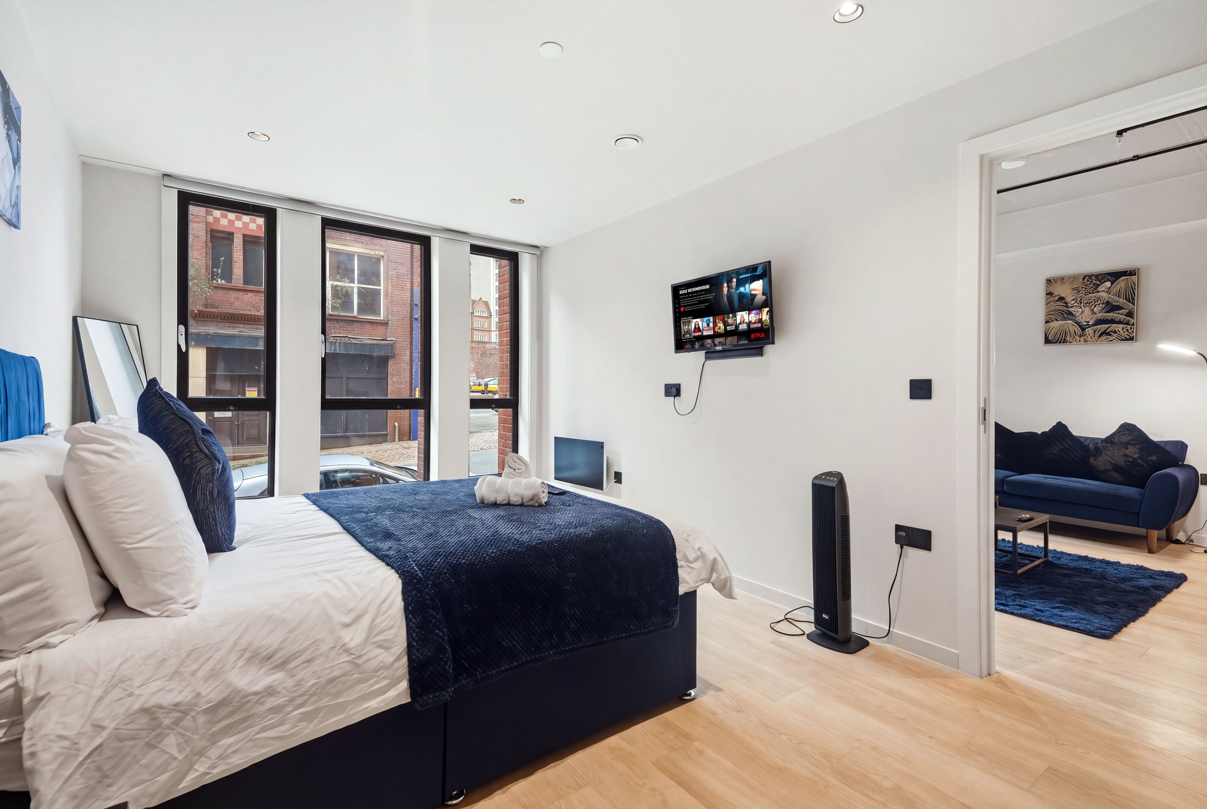 Une chambre à coucher moderne, avec un lit, un téléviseur fixé au mur et une vue sur l’extérieur grâce à de grandes fenêtres.