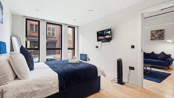 Une chambre à coucher moderne, avec un lit, un téléviseur fixé au mur et une vue sur l’extérieur grâce à de grandes fenêtres.
