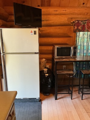 A compact kitchen with a white refrigerator, a microwave, and a small table. - Cute little cabin in the middle of the woods, yet still right in town. (Beaverdell)