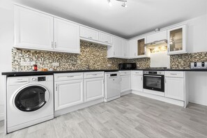 A modern kitchen with white cabinetry, a built-in washing machine, a microwave, and a toaster. - House Sleeps 9 With Enclosed Garden (Solihull)