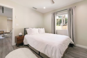 Quarto com cama, mesa de cabeceira e janela com cortinas.