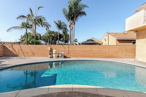 Piscina com muro de tijolos e palmeiras ao fundo.