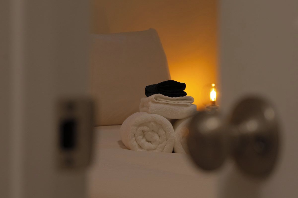 A neatly made bed with rolled towels and a lit candle, suggesting a cozy and well-maintained room.