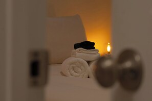 A neatly made bed with rolled towels and a lit candle, suggesting a cozy and well-maintained room.