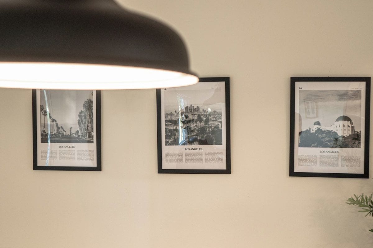 Three framed black and white photographs of Los Angeles on a wall, under a black pendant light.