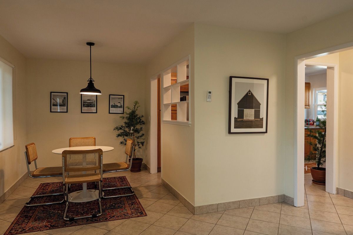 A dining area with a table and chairs, a hanging light fixture, framed pictures on the wall, and a potted plant.