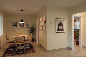 A dining area with a table and chairs, a hanging light fixture, framed pictures on the wall, and a potted plant.