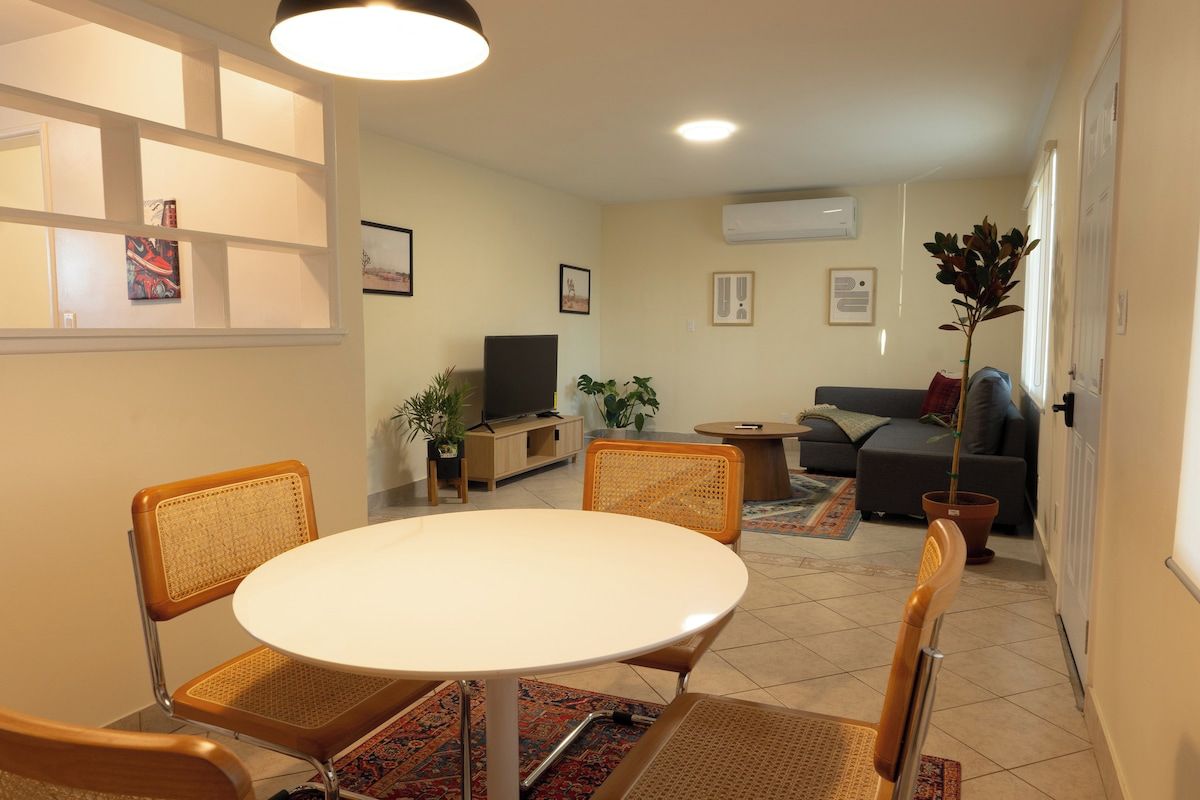 A living room with a round table, two chairs, a sofa, a TV, and a potted plant.