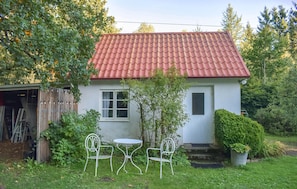 A small house with a red-tiled roof, a front door, and a small garden with two metal chairs and a table. - Beautiful home in Brösarp with WiFi (Brösarp)