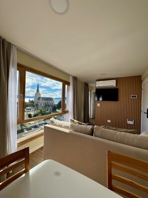 Ein modernes Wohnzimmer mit großem Fenster, Flachbildfernseher und einer Couch.