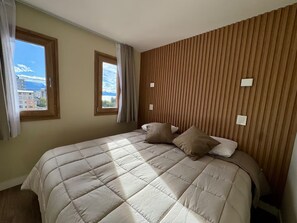 Ein Schlafzimmer mit einem großen Bett, zwei Fenstern und einer Wand aus Holzverkleidung.