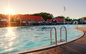 Ein Schwimmbecken mit Metallleiter, umgeben von einer Liegefläche mit Liegestühlen und Sonnenschirmen.