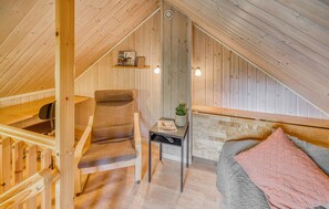 Et hyggeligt soveværelse på loftet med en skrå trævæg, en enkelt seng, en stol, et lille bord med en plante og en reol med bøger.