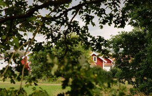 A red barn with a white roof, surrounded by greenery and other buildings in the background. - Beautiful home in Varberg with heated swimming pool (Varberg)