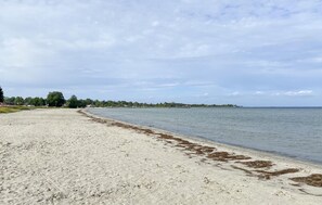 A sandy beach with a calm sea, a distant shoreline with buildings, and a partly cloudy sky. - Lovely apartment in Köpingsvik with sauna (Köpingsvik)