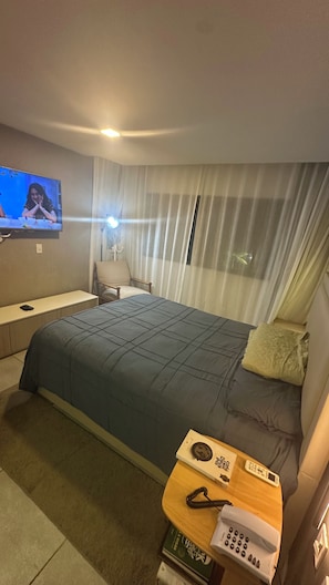 A hotel room with a bed, a TV mounted on the wall, a bedside table with a phone and remote control, and a chair. - Apartment in the luxurious boutique hotel Ritz Suites, fully equipped! (Maceió)
