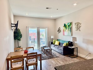 A modern living room with a dining area, a sofa with cushions, a coffee table, and a view through a glass door. - Downtown Chattanooga Condo Overlooking Brewery (Chattanooga)
