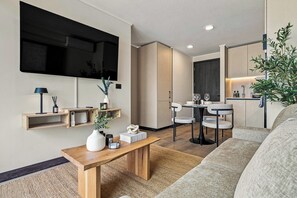 A modern living room with a flat-screen TV, wooden furniture, a dining area, and a kitchen with a plant. - Modern 2BR in Santiago - A/C • Parking • Great Location (Santiago)