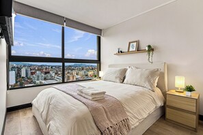 A bedroom with a large window, a bed, a bedside table with a lamp, and a small plant. - Modern 2BR in Santiago - A/C • Parking • Great Location (Santiago)