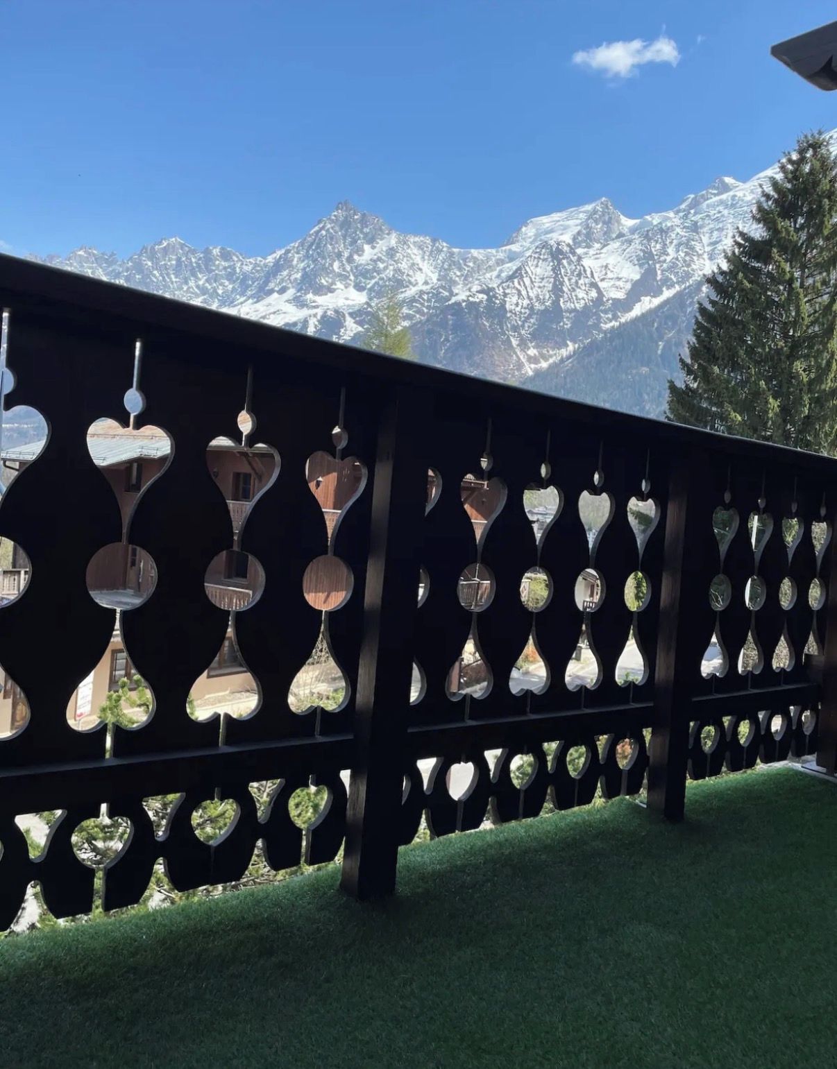 A wooden fence with heart-shaped cutouts, a grassy area, and a mountain range in the background.
