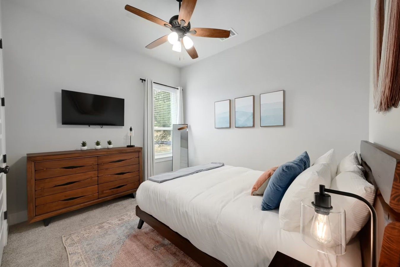 Une chambre à coucher avec un lit, un ventilateur de plafond, une télévision, une commode et des tableaux encadrés accrochés au mur.