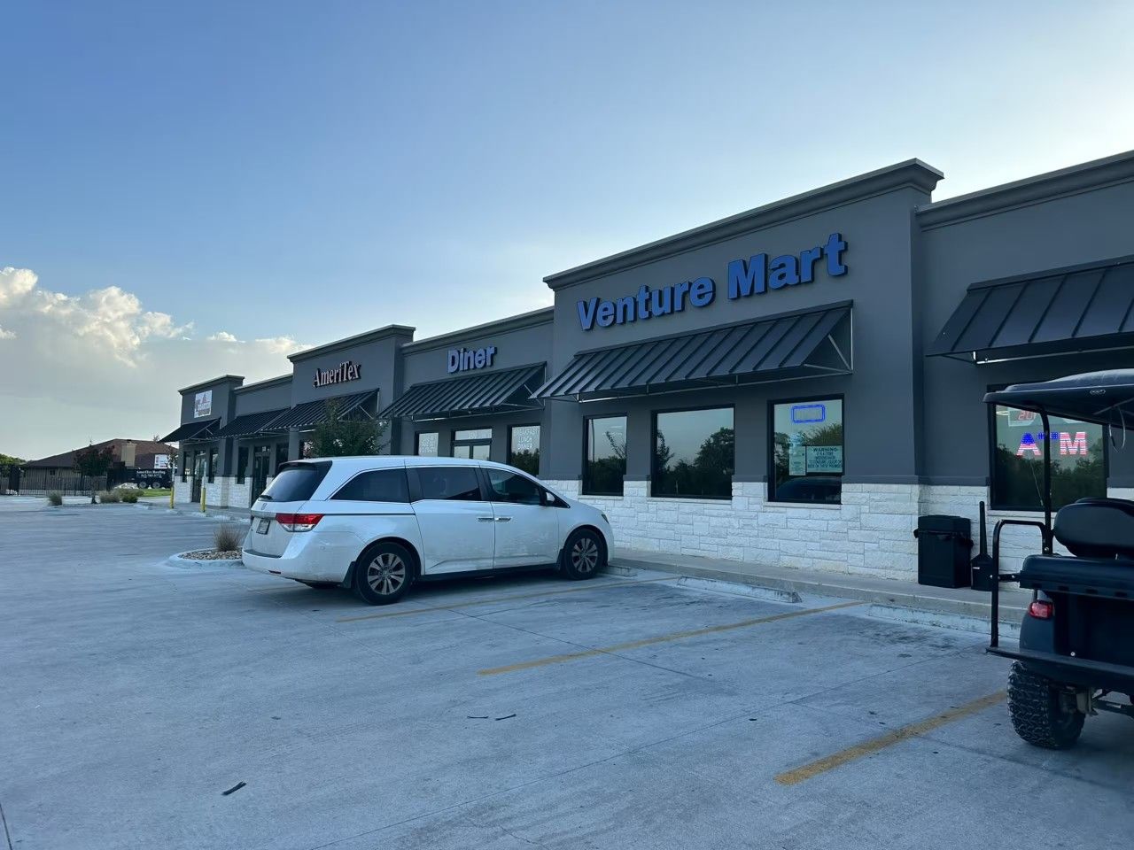 A commercial building with a 'Venture Mart' sign, a 'Diner' sign, and a white car parked in front.