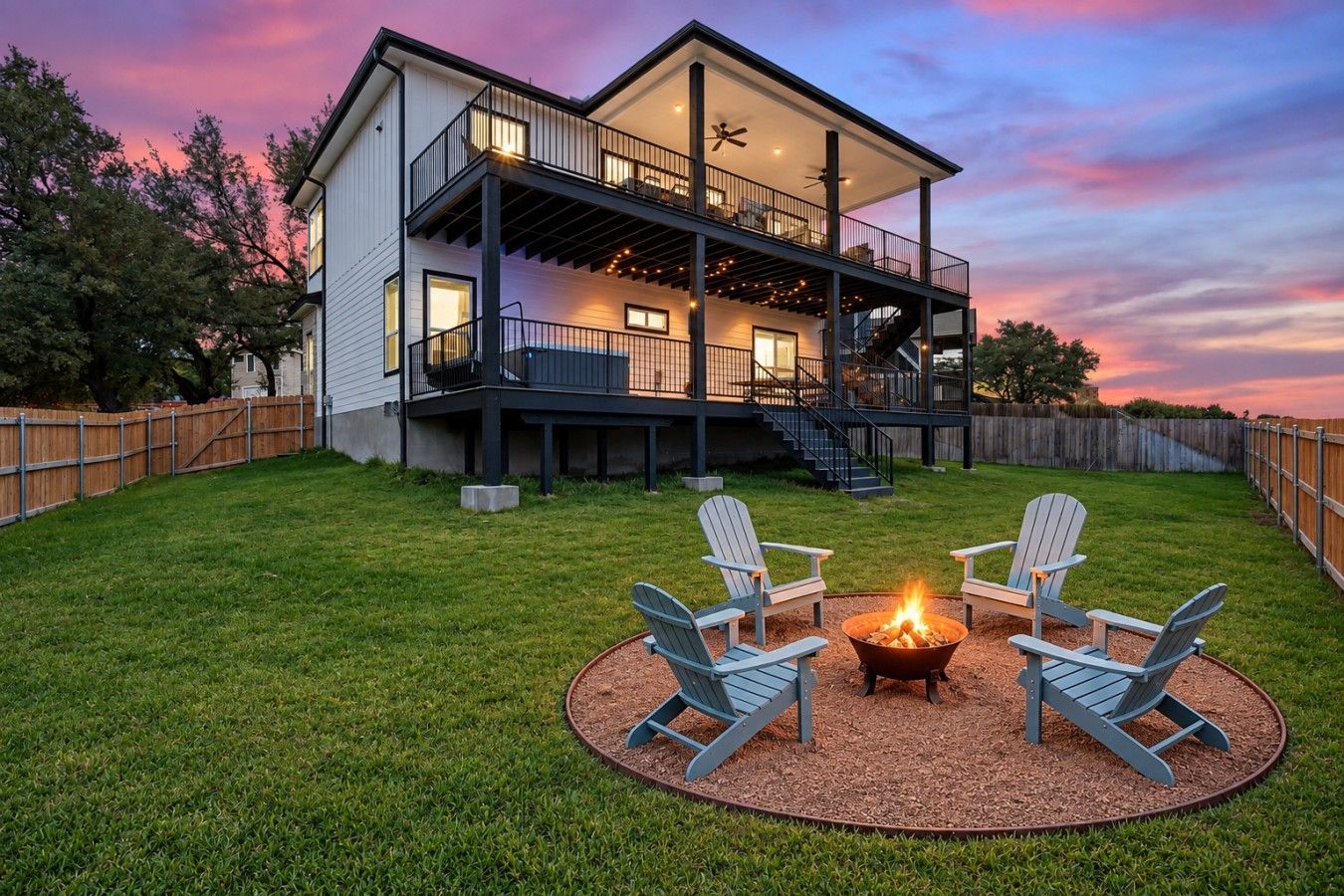 Een tweelaags huis met een balkon, een vuurkorf en twee Adirondack-stoelen.