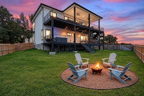 Een tweelaags huis met een balkon, een vuurkorf en twee Adirondack-stoelen.