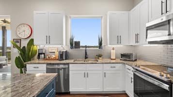 A modern kitchen with white cabinets, a stainless steel dishwasher, a built-in oven, and a coffee station.
