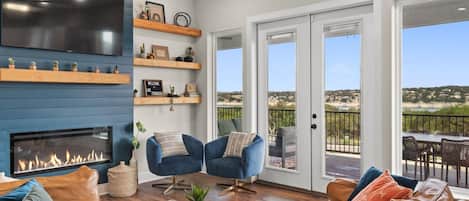 A modern living room with a fireplace, comfortable seating, and a view of the outdoors.