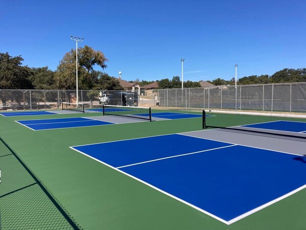 A tennis court with multiple courts, a fence, and trees in the background.
