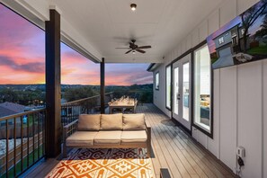 A balcony with a sofa, a dining table set, and a view of the landscape.