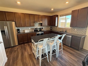 A modern kitchen with wooden cabinets, stainless steel appliances, and a central island with chairs. - Large groups l Family gathering l MCR l RMNP (Loveland)