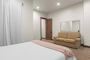 A bedroom with a bed, a sofa, a door, and a mirror. - Summit & Slide Adventure Lodge (Heber City)