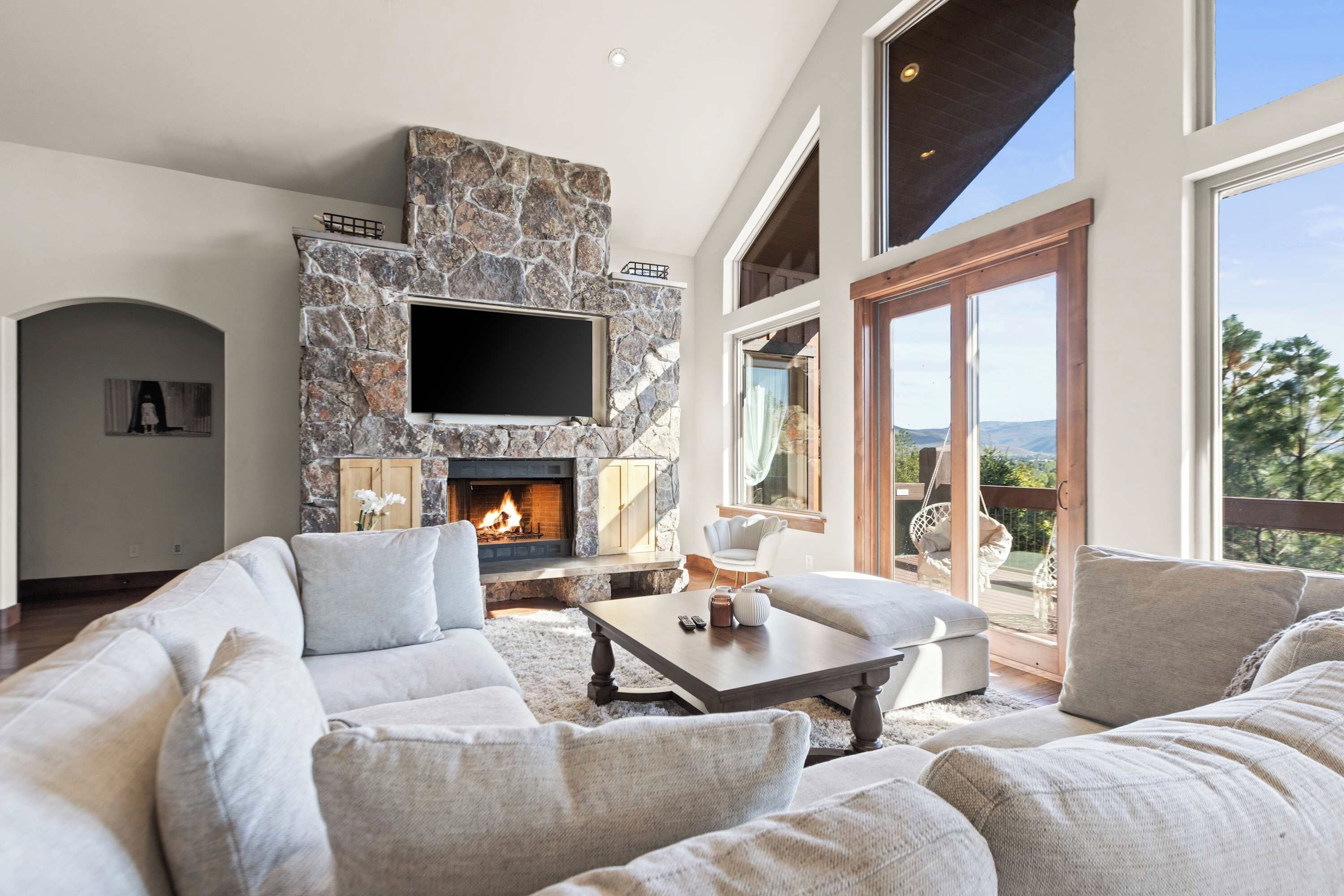 A modern living room with a stone fireplace, a flat-screen TV, and a large window overlooking a scenic landscape.