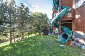 A residential area with a green slide attached to a wooden building, surrounded by trees and a grassy lawn. - Summit & Slide Adventure Lodge (Heber City)