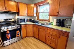 A kitchen with wooden cabinets, a stainless steel stove, a microwave, and a sink. - The Illini House - UIUC Game Day Getaway (Urbana)
