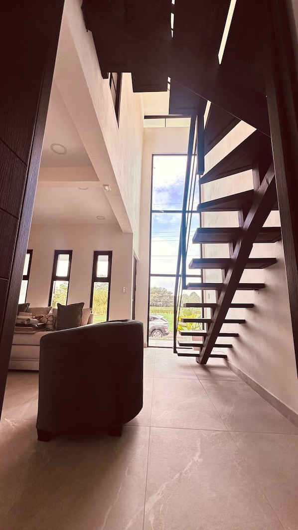 A modern interior with a staircase leading to an upper level, a sofa, and a view of the outdoors.