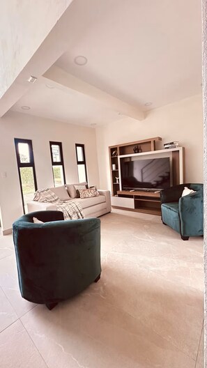 A modern living room with a flat-screen TV, a sofa, and two armchairs.