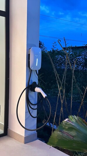 An electric vehicle charging station mounted on a wall with a clear view of the sky and vegetation in the background.