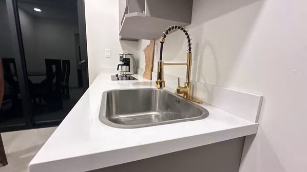 A modern kitchen with a white countertop, stainless steel sink, and a gold faucet.