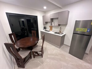 A modern kitchen with a dining table and chairs, a stainless steel refrigerator, and grey cabinetry.