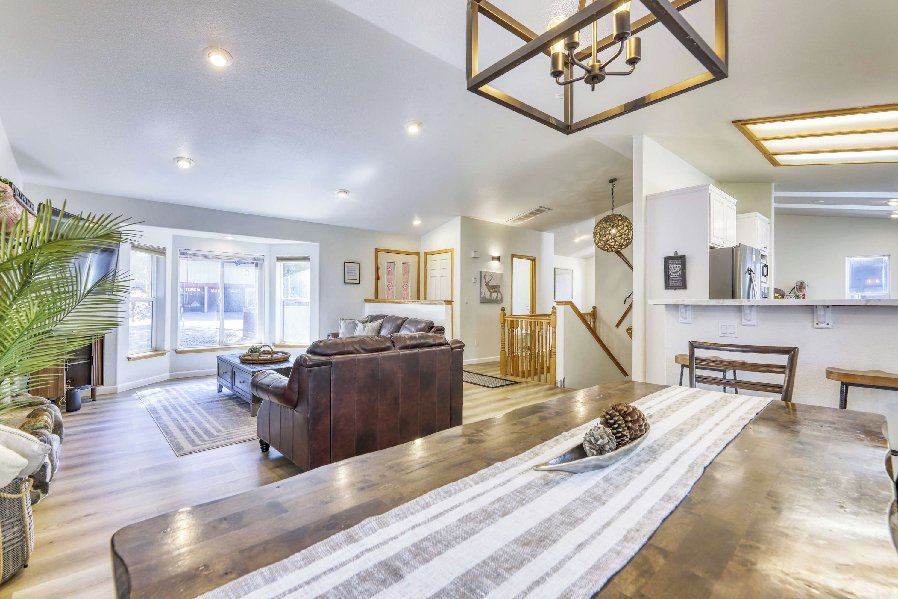 A spacious living area with a wooden dining table, a leather sofa, and a staircase leading to an upper level.